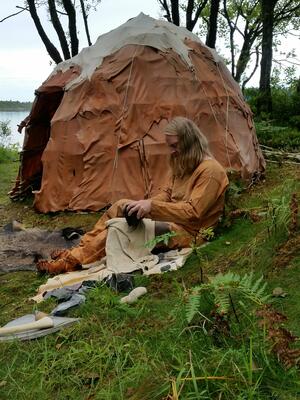 steinalderboplass. Flintsmed knakker flint utenfor steinalderhytte