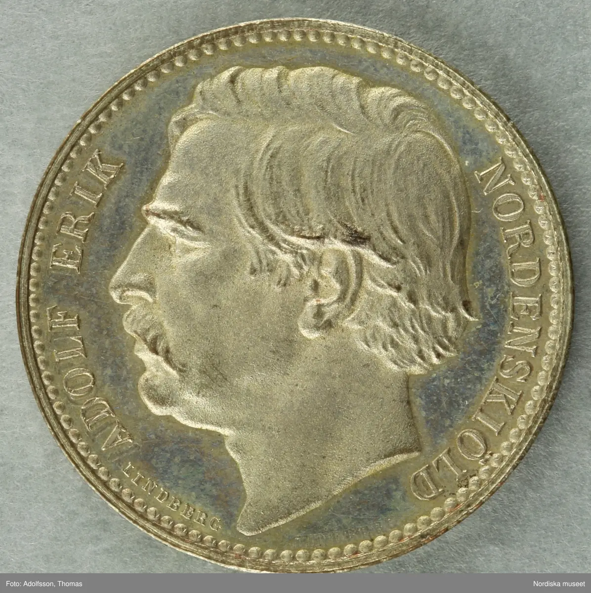 Huvudliggaren:
"Minnespenning, silfver. Öfver Adolf Erik Nordenskiöld. Diam 9 [svårläst] (6te storl.). Åts: 'ADOLF ERIK NORDENSKIÖLD', hufvudet v.s Nederst: 'LINDBERG'. fråns. 'NORDOSTPASSAGEN FULLBORDAD 1878-79.' inom en lagerkrans. Öfverst en strålande nordstjärna. G. af fröken Maria Ruckman i Stockholm 26/1 1895."