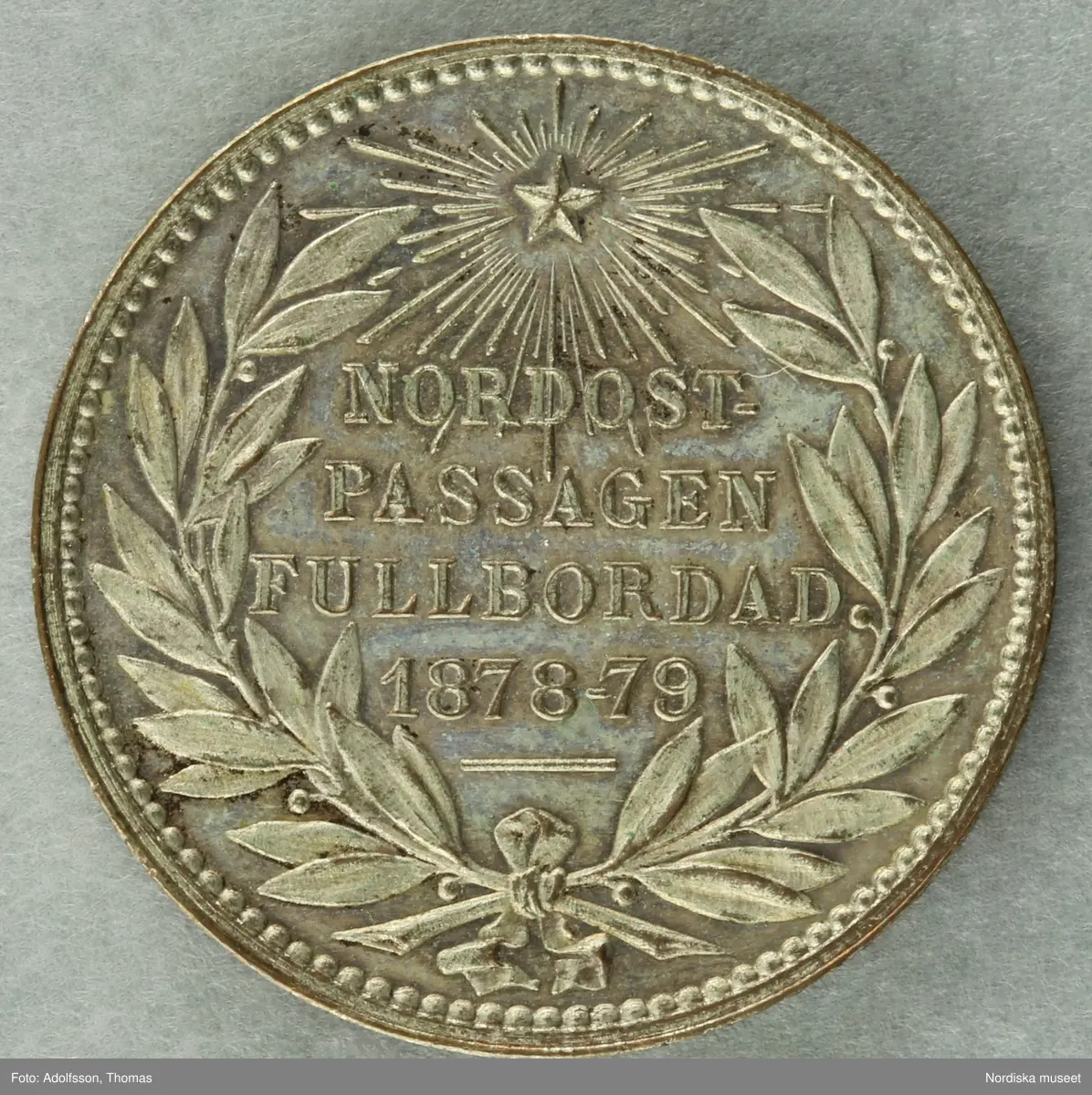 Huvudliggaren:
"Minnespenning, silfver. Öfver Adolf Erik Nordenskiöld. Diam 9 [svårläst] (6te storl.). Åts: 'ADOLF ERIK NORDENSKIÖLD', hufvudet v.s Nederst: 'LINDBERG'. fråns. 'NORDOSTPASSAGEN FULLBORDAD 1878-79.' inom en lagerkrans. Öfverst en strålande nordstjärna. G. af fröken Maria Ruckman i Stockholm 26/1 1895."