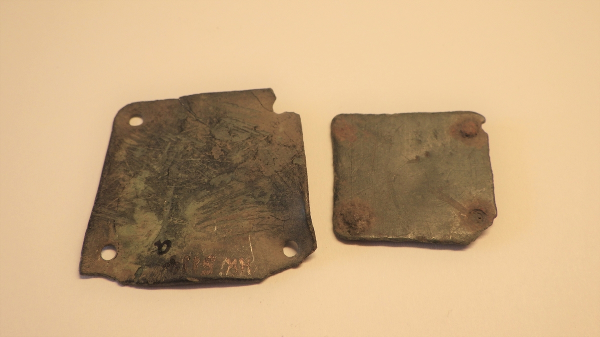 MALV: SE BESK., TILNÆRMET KVADRATISKE PLATER MED AVRUNDEDE HJØRNEROG ET NAGLEHULL I HVERT HJØRNE. A: L. 33 MM, B. 33 MM.  B: L. 25 MM, B. 23 MM, HAR NAGLER AV JERN SITTENDE PÅ PLASS.