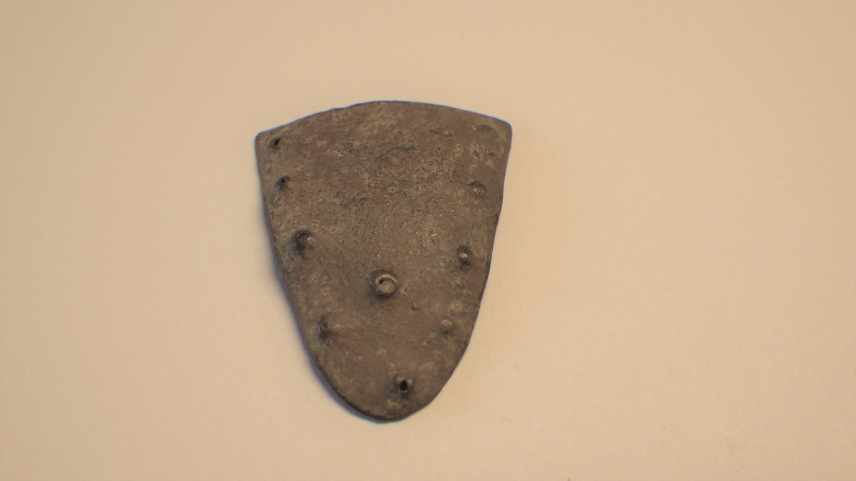 Dekor med punslede punkter i linje langs de to lengste kantene. 4 på hver side som møtes i et femte punkt på spissen. I tillegg et punkt på midten av gjenstanden.