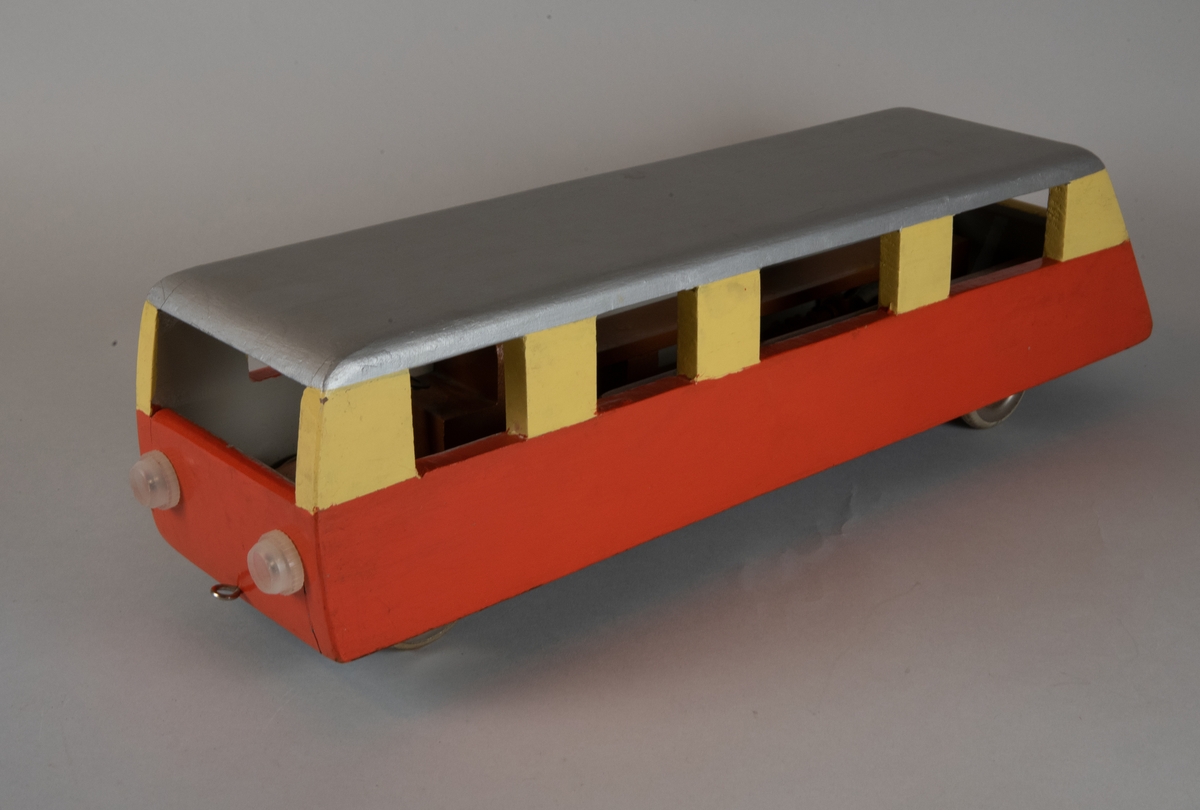 Leksaksrälsbuss av trä med plastlyktor framtill och plasthjul. Rälsbussen är målad nedtill i orange och upptill i ljusgult med silvergrått tak och svart undertill. Rälsbussen är inredd med fasta träbänkar på sidorna samt en förarstol och ratt. Föregångaren är Trafikförvaltningen Göteborg Dalarna Gävles rälsbuss XaXm.