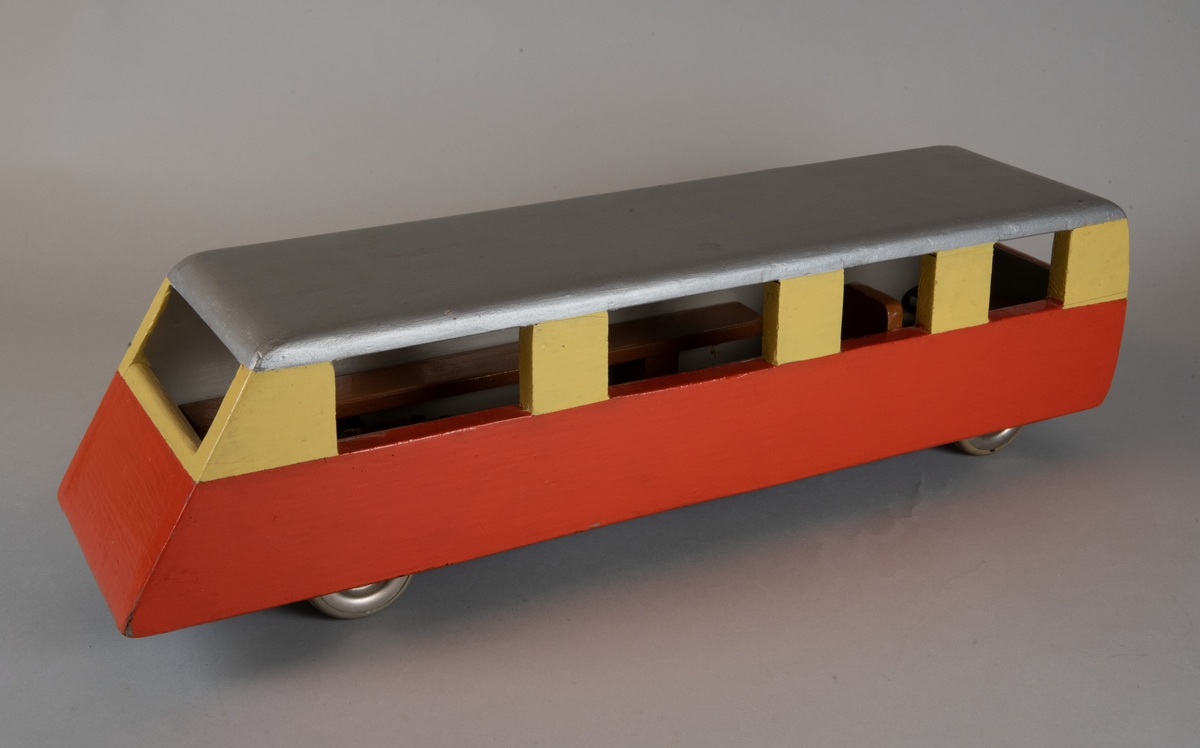 Leksaksrälsbuss av trä med plastlyktor framtill och plasthjul. Rälsbussen är målad nedtill i orange och upptill i ljusgult med silvergrått tak och svart undertill. Rälsbussen är inredd med fasta träbänkar på sidorna samt en förarstol och ratt. Föregångaren är Trafikförvaltningen Göteborg Dalarna Gävles rälsbuss XaXm.