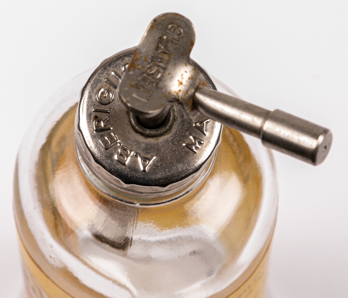 Glasflaska med pump av metall. Gul etikett men texten "Glansett". Har innehållit putsmedel till blanka ytor som glas och kakel.