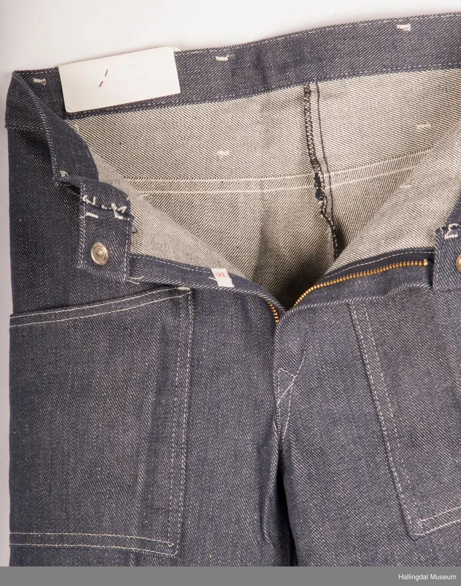 Mørk blå slengbukse i dongeri. Lavt liv.  Påsydde utvendige lommer foran og bak.  Metallglidelås i gylf.