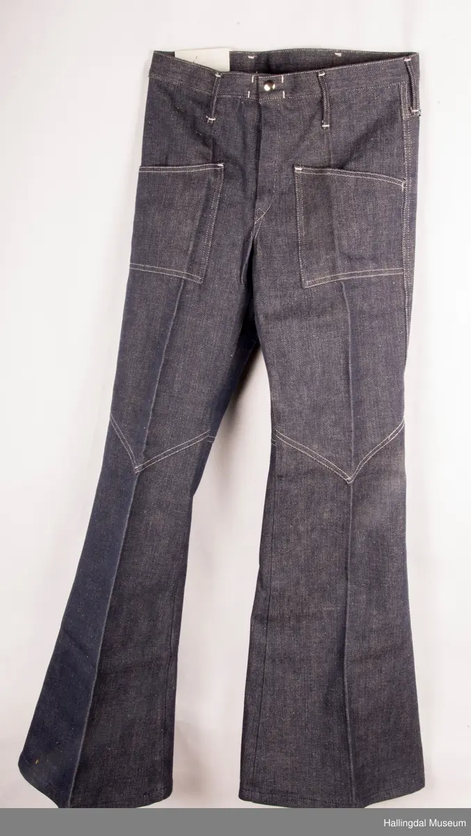 Mørk blå slengbukse i dongeri. Lavt liv.  Påsydde utvendige lommer foran og bak.  Metallglidelås i gylf.