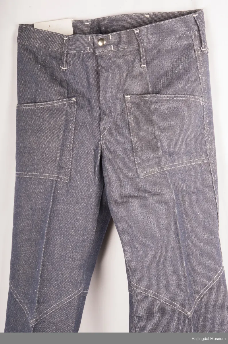 Mørk blå slengbukse i dongeri. Lavt liv.  Påsydde utvendige lommer foran og bak.  Metallglidelås i gylf.