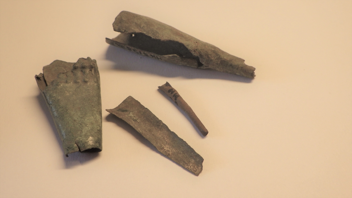 MALV: L. (MM): A: 54, B: 41, C: 34, D: 24, EMNER OG DELVIS FERDIGE BESLAG AV TYNT BRONSEBLIKK. TREKANTEDE PLATER MER ELLER MINDRE SAMMENRULLET. A: HAR TO NAGLEHULL, B: HAR PUNKT OG STREKORNAMENTIKK, MULIG NAGLEHULL, C: ER ET IKKE SAMMENRULLET EMNE, D: ER HELT SAMMENRULLET. 