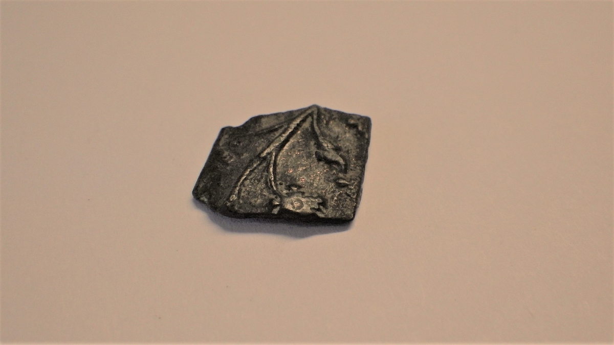 MALV: H. 11 MM B. 12 MM, LITEN, SVAKT BUET PLATE. AVBRUKKET PÅ TO SIDER. OPP-HØYET PLANTEORNAMENTIKK. 