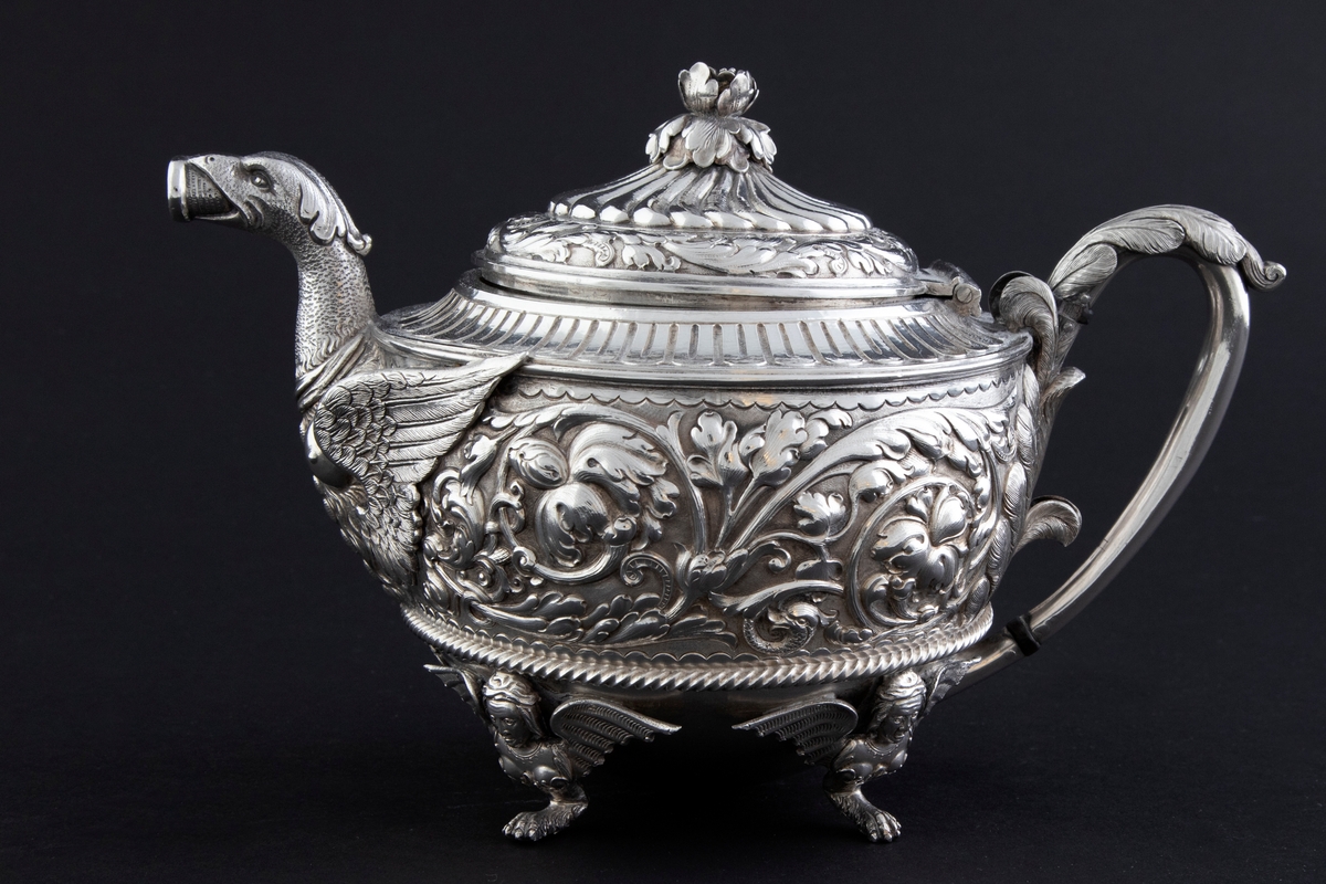 Tekanne i sølv. Tilhærmet halvkuleformet korpus, dekorert med rankeornamenter i relieff. Opprinnelig har overflaten mellom rankene vært oksidert. Kannen bæres av fire små ben, utformet som harpyier-lignede vesener, hvor vingene utgjør ansatsen til korpus. Svungen hank med plastisk utformet bladornament, samt tut med en griffelignende utforming. Sirkulært hengslet lokk med konsentrisk plastisk dekor og blomsterformet lokknapp.