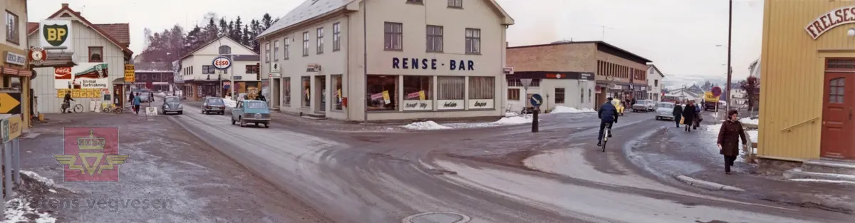 Brumunddal i Ringsaker, Hedmark. Mars 1974. 
Sentrum med fotgjengere og syklister på fortau og gate. BP og Esso bensinstasjon.