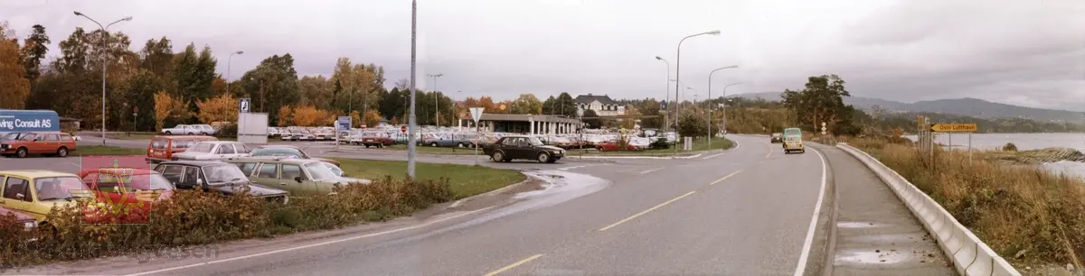 Riksveg 166 Snarøyveien x Martin Linges vei. Riksveg 166 fra syd. Skilt viser Oslo Lufthavn Fornebu. Oktober 1980.
Bevoktet parkering og stor parkeringsplass.  Skilt med "Bruk Bilbelte."  
En Saab 99 kjører ut fra Martin Linges vei og ut på riksveg 166 Snarøyveien.