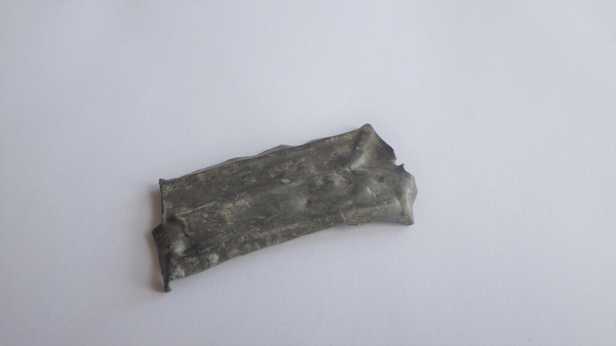 MÅL: L. 46 MM B. 25 MM, TILNÆRMET REKTANGULÆRT, ENE SIDEN NOE BUET. KANTENE ER OPPHØYET. Y-FORMET ORNAMENT GÅR LANGS HELE BESLAGETS LENGDE. TO NAGLEHULL.