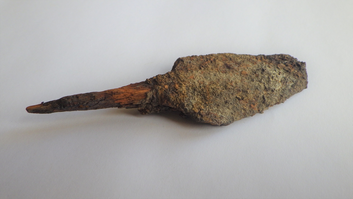 MÅL: L. 112 MM B. 32 MM, BLADFORMET SPISS MED TANGE. INGEN TYDELIG MIDTRYGG. SPOR AV TREVERK VED ROTEN AV BLADET (TILNÆRMET RYGH 547). Spissen brukket.