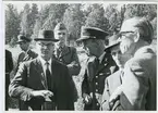 Befäl vänder sig till civilklädd man i hatt.