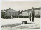 Officer med sorgband står framför flera militärled
med vit fana på kasernområdet I 4.
