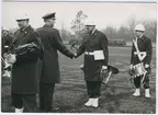 Officer hälsar på militärmusiker.Militärer under marsch längre bort.