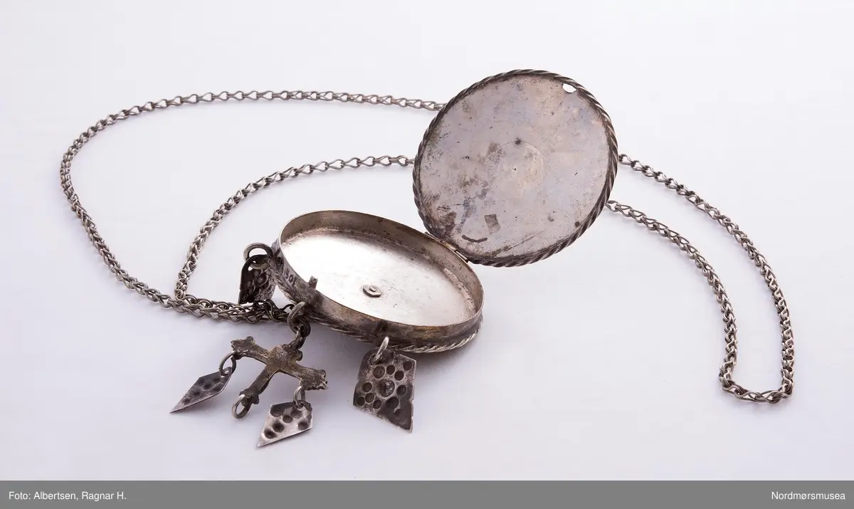 Lavendeldåse med gitterverkblomst på lokket og feste for lenka. Fra dåsen henger løv og et krusifiks med løv. Kjeden har karabinkrok.