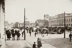 Stortorget, Växjö, hörnet Storgatan / Kungsgatan, 1895. En torgdag med mycket folk i rörelse. Till höger syns dåv. stadshuset och snett bakom detta några av husen i kvarteret Lejonet vid Kronobergsgatan, bl a J.E. Bergs fastighet. Bakom dem syns domkyrkans torn. Långt i bakgrunden skymtar gårdsbebyggelsen vid Östregård.