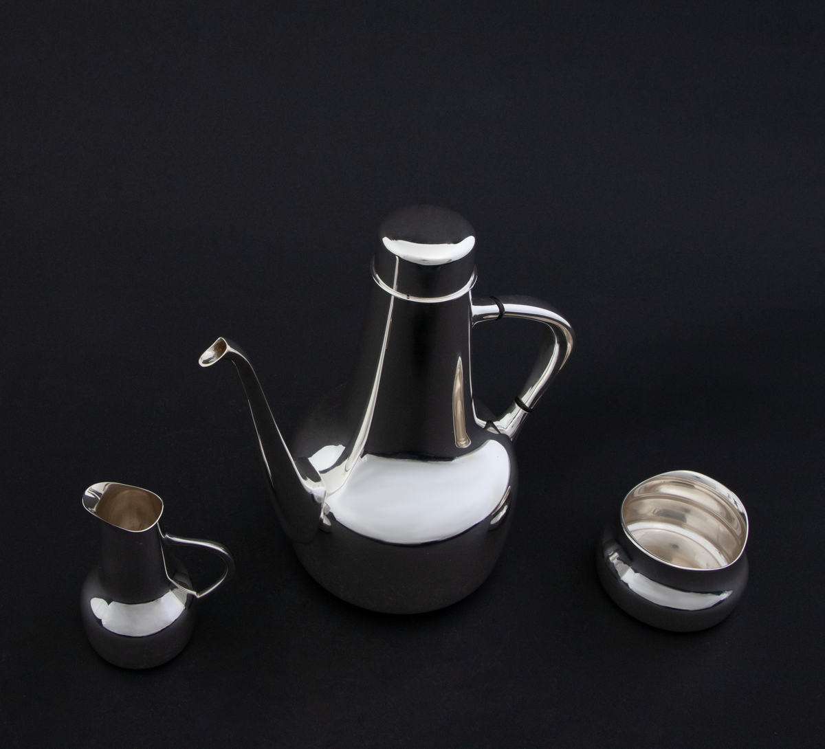 Kaffeservise i tre deler, utført i sølv. Samtlige deler er glattpolert, uten dekor og med mykt avbuede kanter. 

1) Kanne med sylinderformet kompakt korpus, som glir over i en konisk langstrakt hals. Fra korpus løper en lang tynn tut, som er mykt buet. Det sirkulære lokket fremstår som en forlengelse av halsen, men overgangen er markert med en ringformet vulst. Den buede haken løper fra korpus til øvre del av halsen, og før ansatsene er det plassert to ringformede lameller av presstoff for varmeisolering. 

2) Fløtemugge med sylinderformet kompakt korpus, som glir over i en konisk langstrakt hals, som avsluttes i et nebb. Muggens buede hank løper fra korpus til midten av halsen.Sukkerkopp med oval grunnform, og buet kant øverst. 

3) Sukkerkopp med oval grunnform, og buet kant øverst.