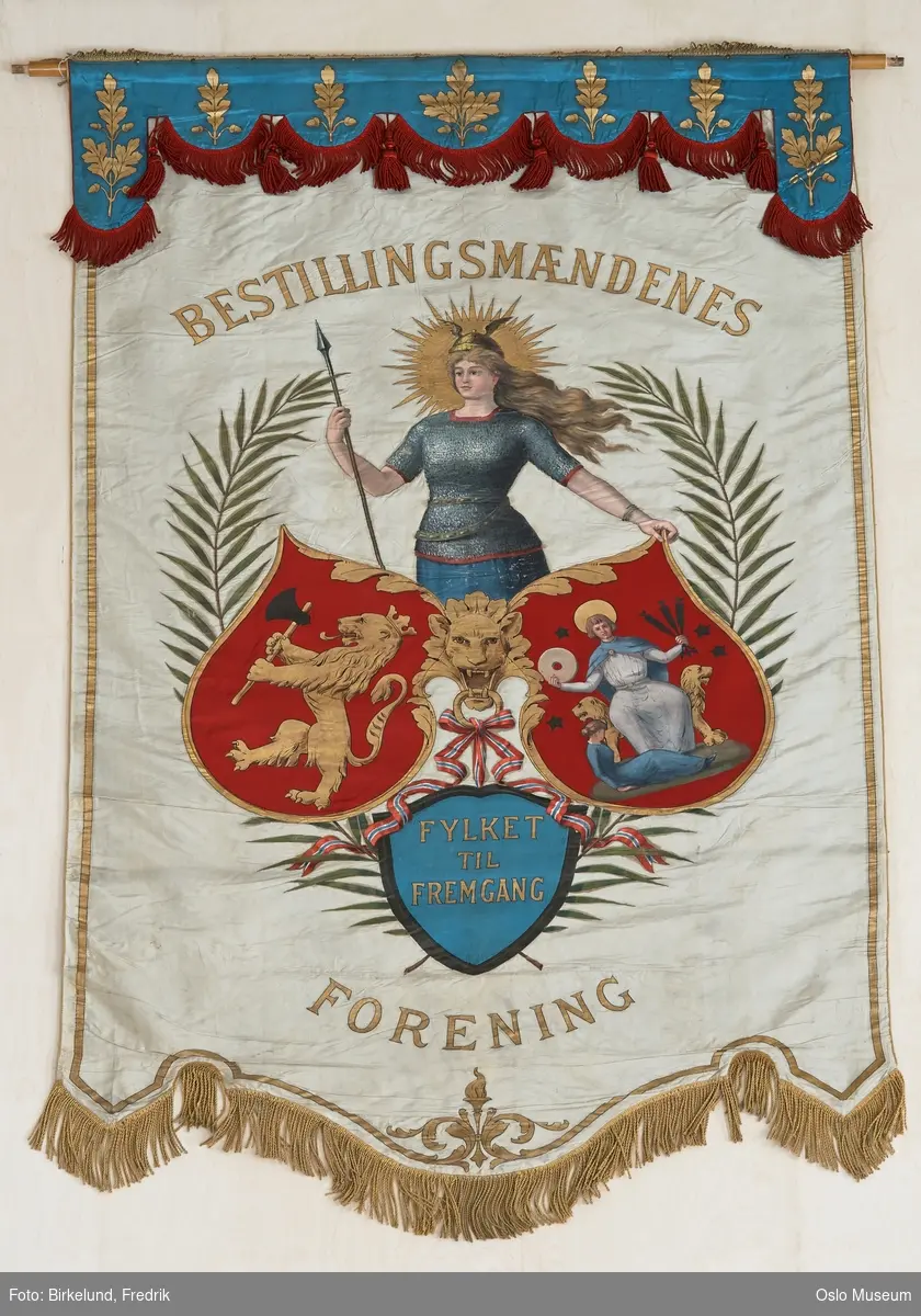 A: Gullmalt hovedspir til fane.
D-E: Gullmalte sidespir til fane.
F: faneduk, duk av dobbel silke festet til tverrstang med messingstifter på possement med gul silkefrynse. Dukens forside av av hvit silke med øverst; blå, tunget kappe med malte eikeblader i gull. Kantet med rød silkefrynse. På midten malt, polykromt motiv, delvis applikert: valkyrie ståver over tre skjold, to med rød bunn og ett med blå. I de røde skjoldene henholdsvis den norske løve og St. Hallvard. I det blå innskrift i gullskrift. Mellom skjoldene båndsløyfe i rødt/ blått/ hvitt. På sidene palmegrener. Dukens nedkant tunget med gul silkefrynse, langs sider og nedkant malt gullstripe, nederst med akantus og flamme. Over og under midtmotivet insripsjon med gullbokstaver. På baksiden: blå silke med malt gullbord som på forsiden og innskrift med gullbokstaver.