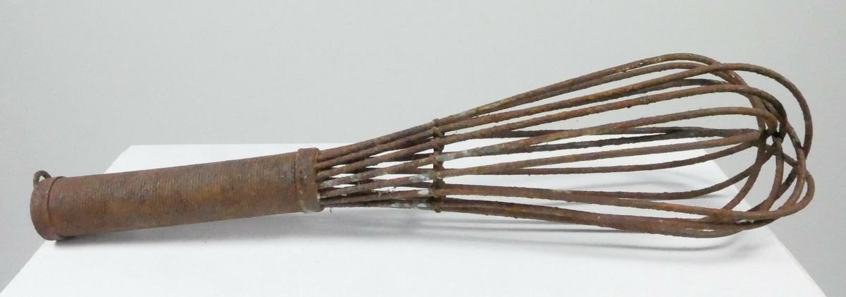 Visp av metall med åtte bøyde metalldeler. Rundt håndtak av metall. 