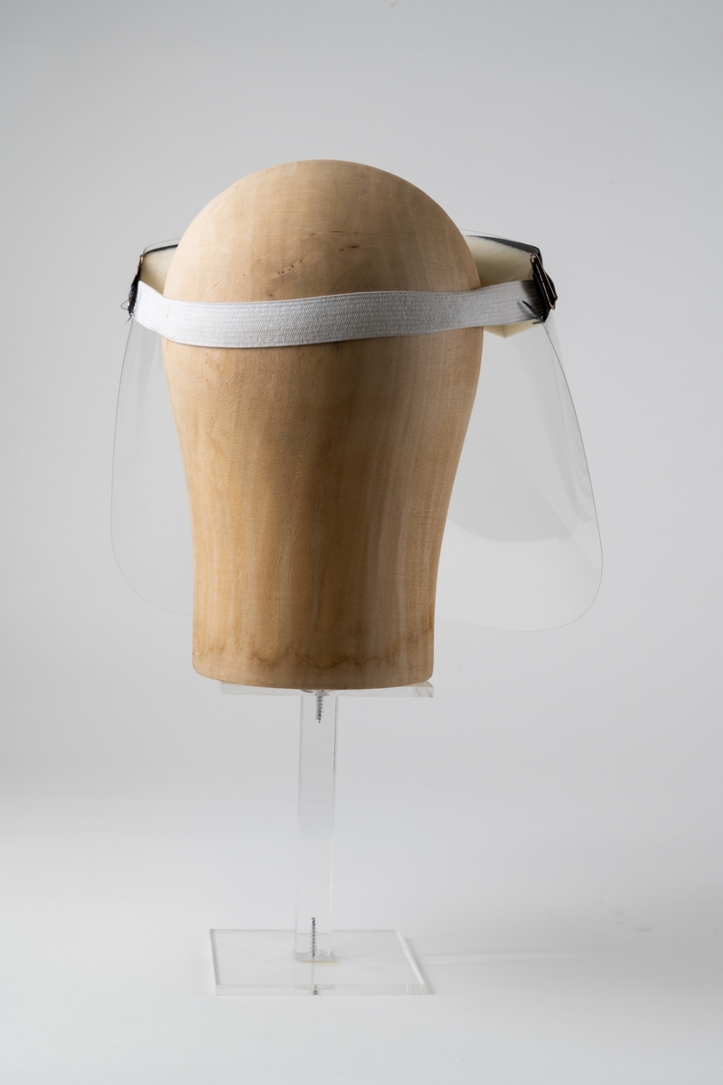 Visir av genomskinlig plast, heltäckande för ansikte. Ett avlångt stycke skumplast är fäst på baksidan av övre kanten på visiret, för placering mot pannan. Visiret hålls på plats med elastiskt resårband mot bakhuvudet. Resårbandet är fäst i visiret med en metallklammer i var sida. Över skumplastremsan är ett svart band med guldtexten "Interflora" fäst med gem i var ände. På skumplasten är textat: "P", vilket betyder Pelle, visirets användare.

Artikelnummer: ZSKYVIS0003.

Se vidare Historik.