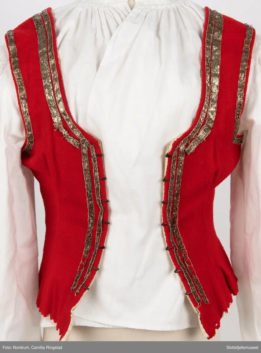 Liv med innsydde spiler. Hekter på hver side av åpningen foran. Gyldne bånd påsydd 