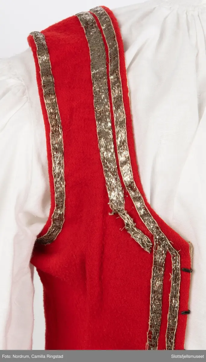 Liv med innsydde spiler. Hekter på hver side av åpningen foran. Gyldne bånd påsydd 