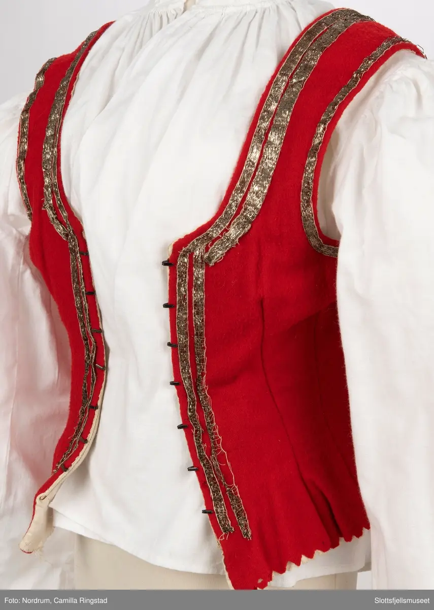 Liv med innsydde spiler. Hekter på hver side av åpningen foran. Gyldne bånd påsydd 