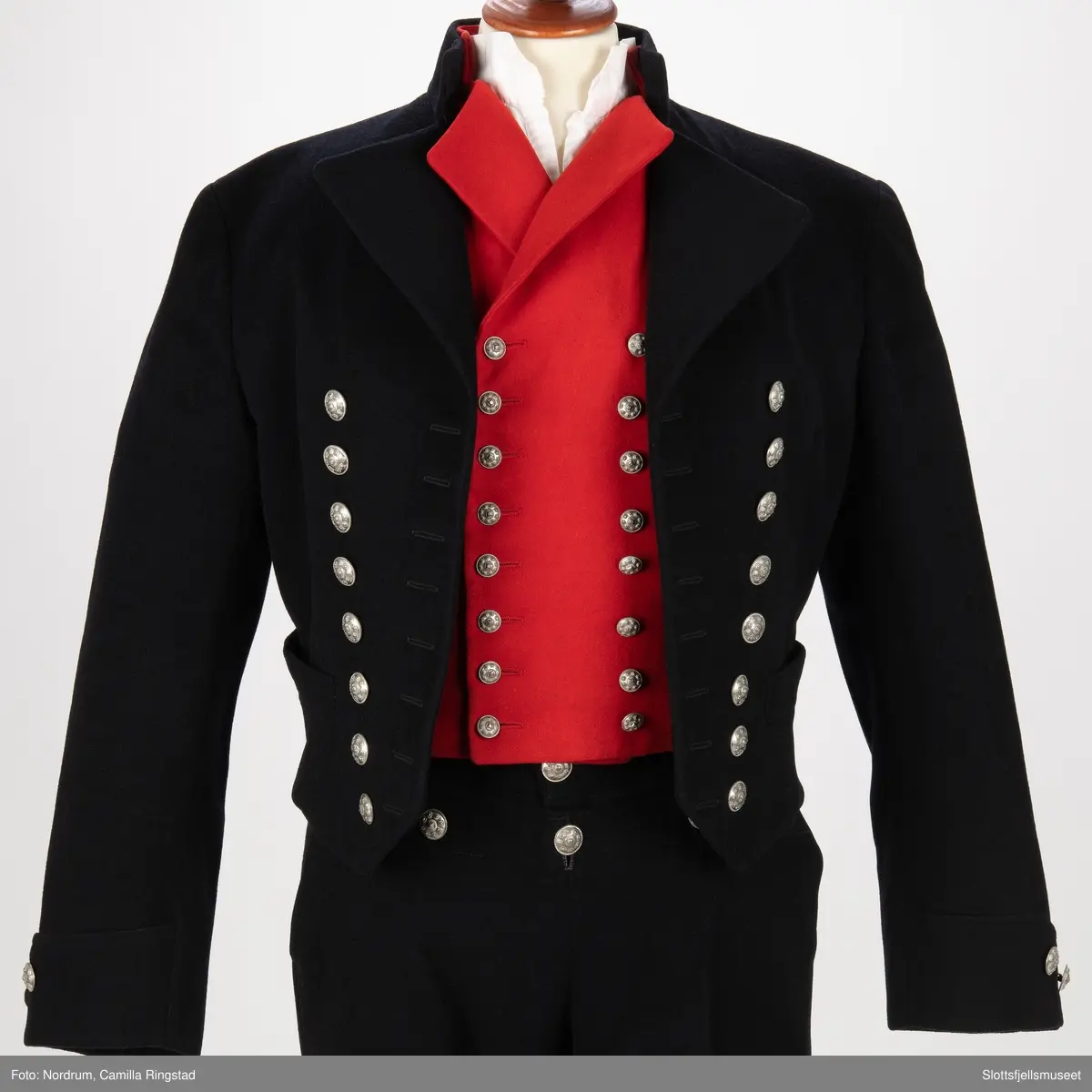 Svart jakke med dobbelrekke knapper. Sølvknapper på lukkingen og på ermene.