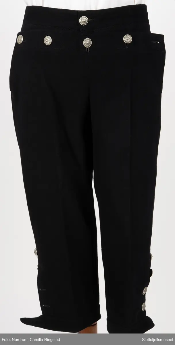 Svart draktbukse med sølvknapper på bein og ved lukkingen.