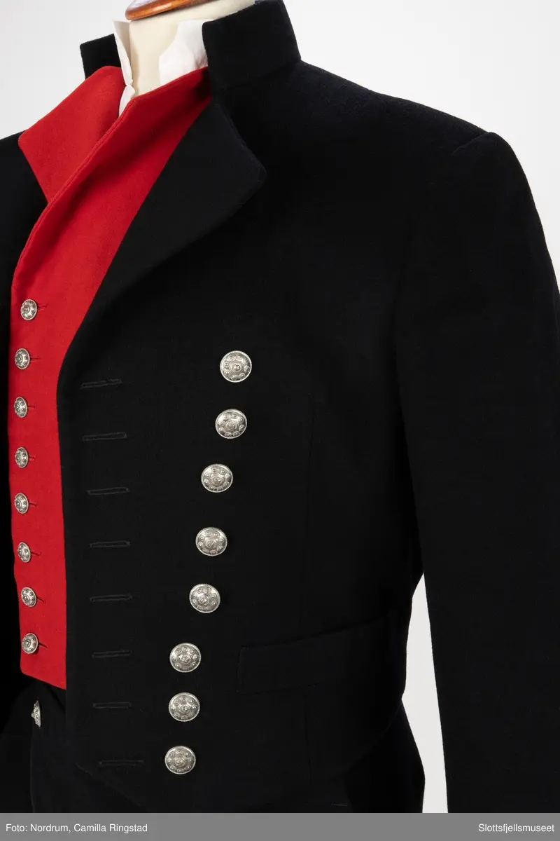 Svart jakke med dobbelrekke knapper. Sølvknapper på lukkingen og på ermene.