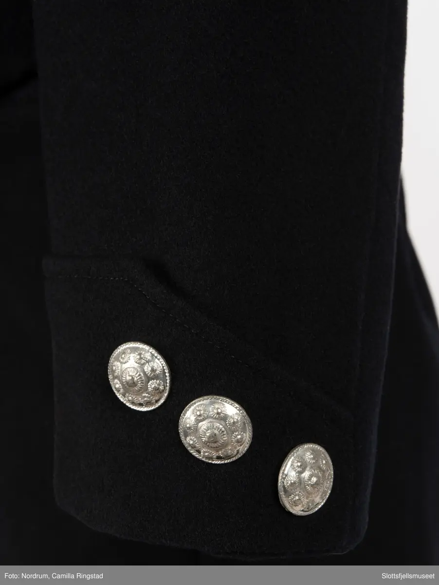 Svart jakke med dobbelrekke knapper. Sølvknapper på lukkingen og på ermene.