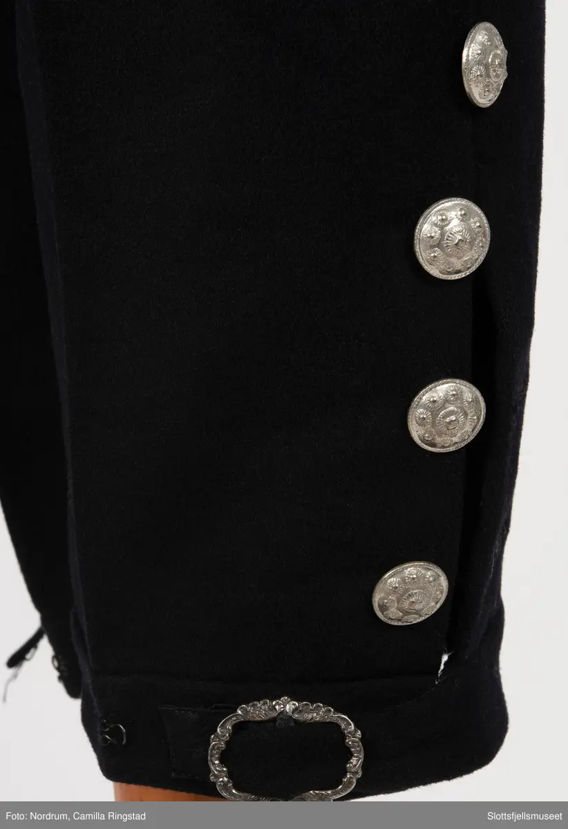 Svart draktbukse med sølvknapper på bein og ved lukkingen.