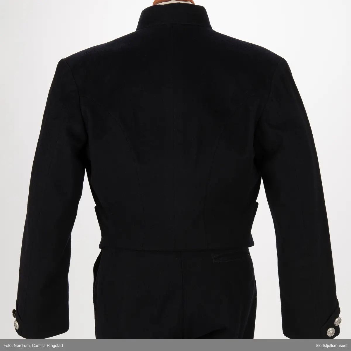 Svart jakke med dobbelrekke knapper. Sølvknapper på lukkingen og på ermene.