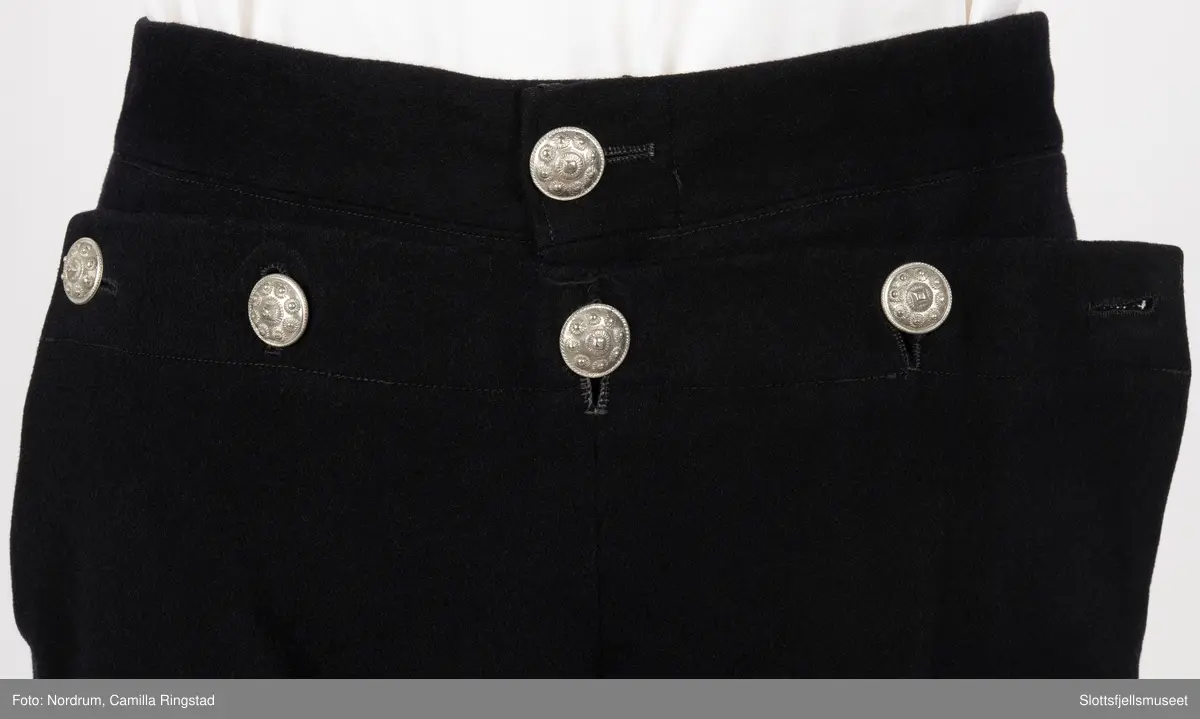 Svart draktbukse med sølvknapper på bein og ved lukkingen.