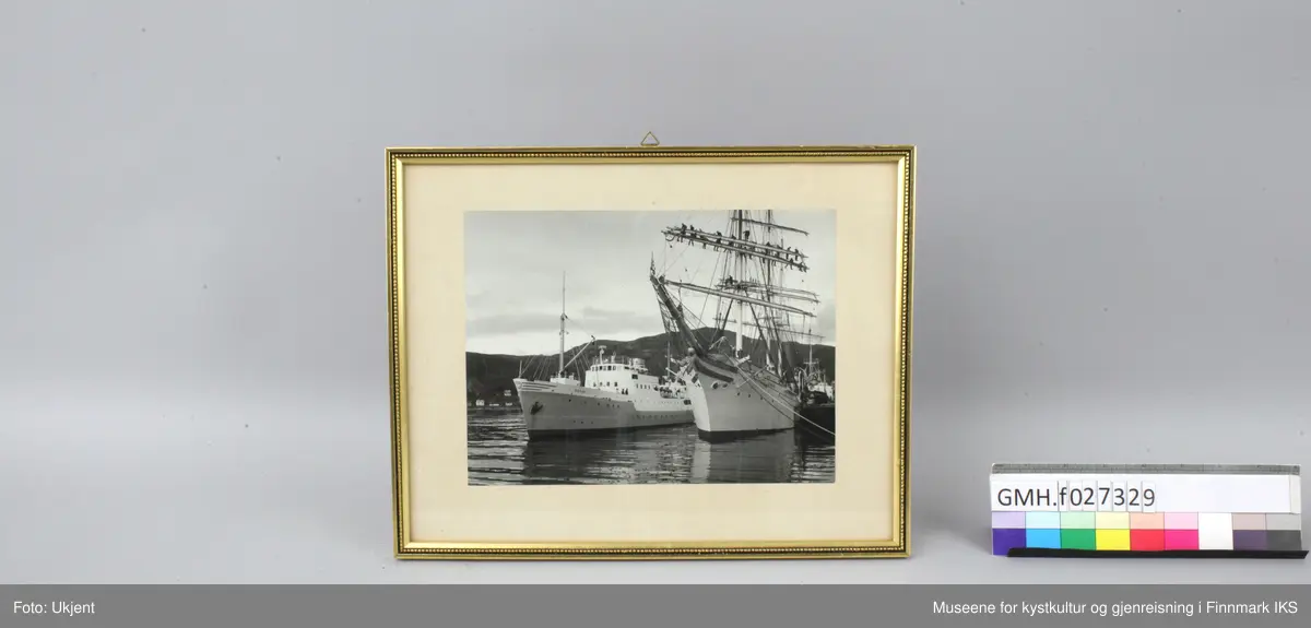 FFR - båten M/S Sørøy og tremasteren "Statsraat Lehmkuhl" ligger i havna i Hammerfest. Ombord på rutebåten står flere personer og ser på hav som foregår på den store seilbåten. Der står det mange personer på bommene.