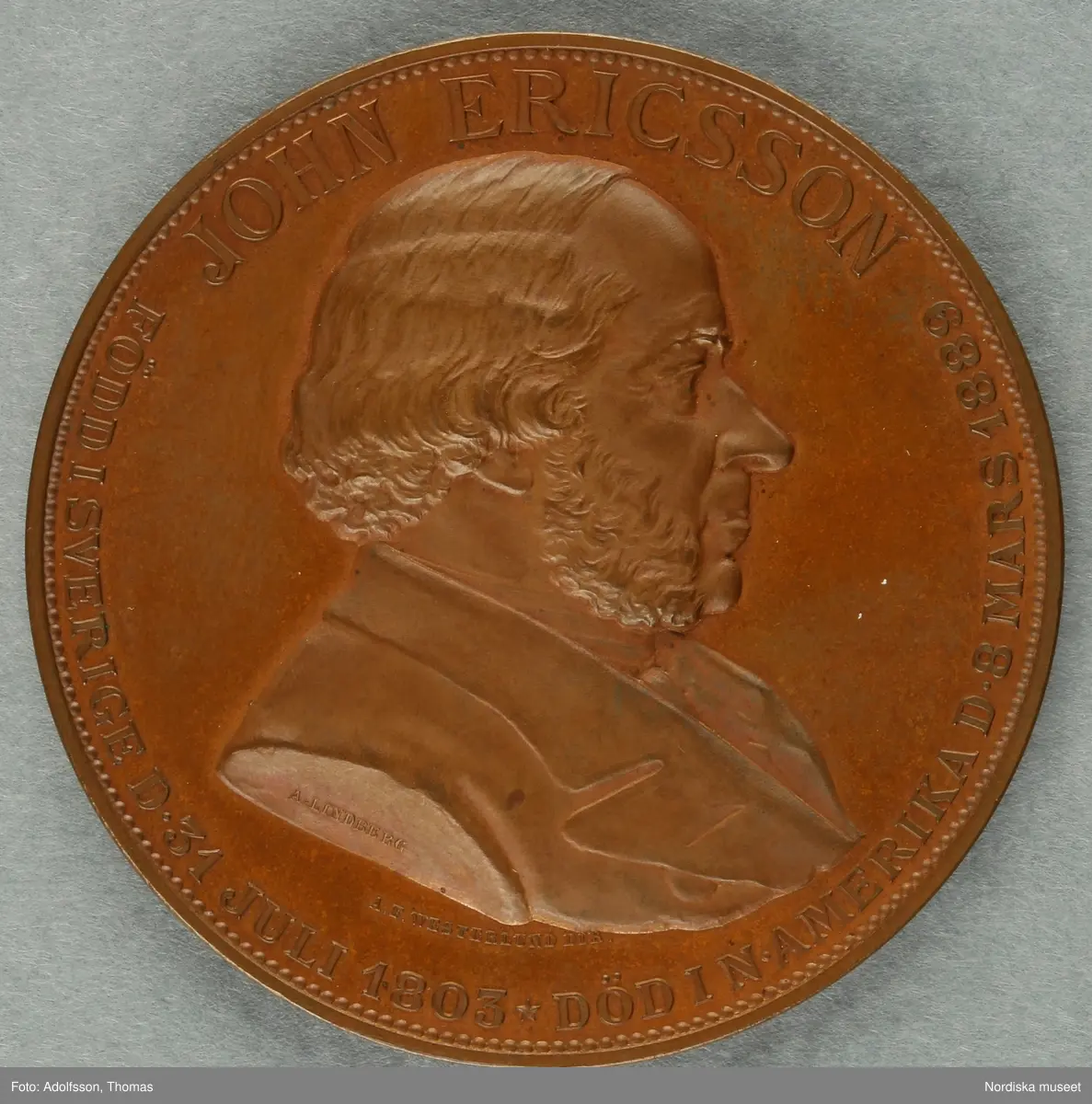 Huvudliggaren:
"Minnespenning. I koppar. Å åtsidan löses 'JOHN ERICSSON FÖDD I SVERIGE D. 31 JULI 1803 * DÖD I N AMERIKA D. 8 MARS 1889.', 'A. LINDBERG', 'A.F. WESTERLUND DIR.', å framsidan: 'TILL MINNE AF DEN FRÄJDADE UPPFINNAREN 1890'.
G. af ingeniör A. F. Westerlund i Stockholm 12/10 1890."