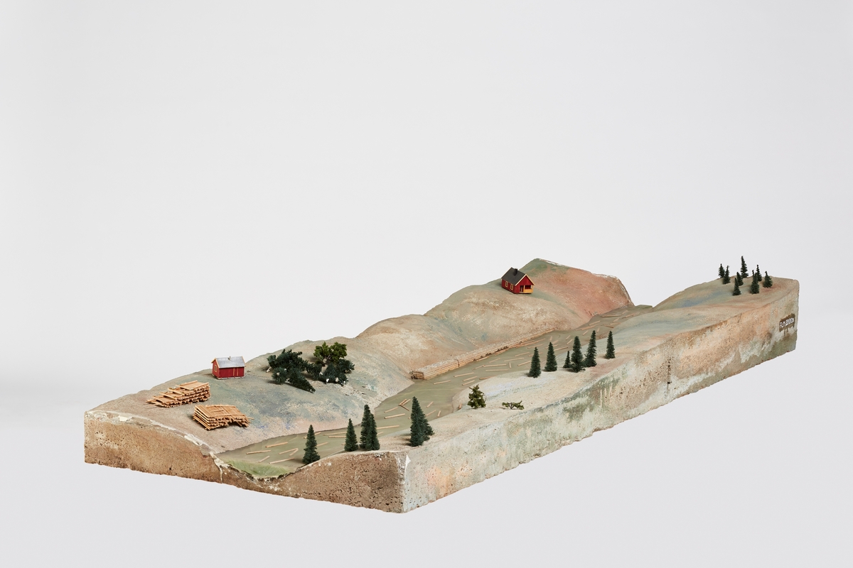 Seksjon to ovenfra (oppstrøms) av modell i fire fysiske seksjoner (FLM.002000).

Modellen som helhet gjengir et elveløp med ulike fløtingsrelaterte bygningselementer (dam, forbygninger, steinkar, lenser, bygninger og broer) og situasjoner (lunnet tømmer, tømmer som fløtes, tømmervaser). Modellen illustrerer ikke et reelt elveløp, men bygningselementene kan være basert på eksisterende sådan. Skala er ikke angitt, men kan beregnes omtrentlig.

Overflaten gjengir en landskapskontur med elvebunn. Elvebunnen er fylt med "vann" i form av et plastmateriale. Landoverflaten er malt i grå og grønne valører for å illustrere berggrunn, løsmasser og vegatasjon. Modelltrær er limt på overflaten. Trepinner er limt på vannflaten for å illustrere tømmerstokker. Det er tre bygninger på modellen - et større bolighus, en mindre hytte eller koie, og en flytende hvilebrakke.

Seksjon en (FLM.002000.A) viser en dam (nåledam) med bilvei over og forbygninger langs elvebredden nedenfor dammen samt et gult bolighus.

Seksjon to (FLM.002000.B) viser laftet, steinfylt forbygninger som avsperrer små viker og et par tømmerlunner.

Seksjon tre (FLM.002000.C) viser en koie med et par robåter på elvebredden, en laftet, steinfylt forbygning som avsperrer en evje og en tømmervase.

Seksjon fire (FLM.002000.D) viser en vei som krysser elven via en fagverksbro, en attholdslense med fem rierkar og en hvilebrakke.