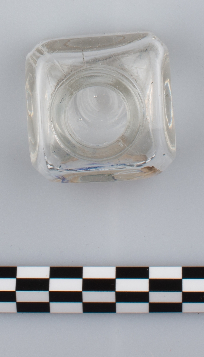 Blank, tom flaske i klart glass uten skrulokk. del av etikett på en side. Rester av blå substans på innsiden. Etiketten har orange bakgrunn