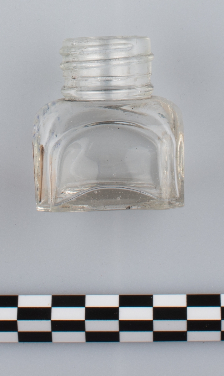 Blank, tom flaske i klart glass uten skrulokk. del av etikett på en side. Rester av blå substans på innsiden. Etiketten har orange bakgrunn