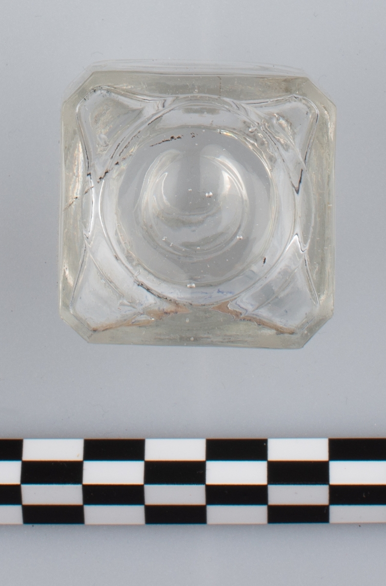 Blank, tom flaske i klart glass uten skrulokk. del av etikett på en side. Rester av blå substans på innsiden. Etiketten har orange bakgrunn