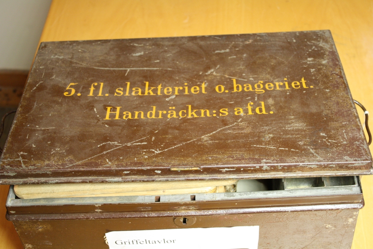 Expeditionslåda av plåt med svart lock. 2 handtag på kortsidorna.
Mörkbrun med målad text på locket i gult: "5. fl. slakteriet o. bageriet. Handräckn:s afd."
Invändigt försedd med påklistrad innehållsförteckning. Innehåller dock inget materiel.