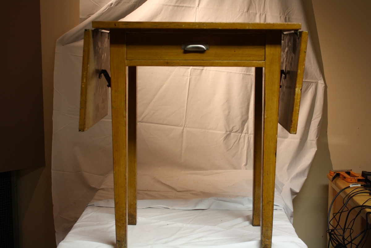 Enligt kartotek: Skrivmaskinsbord, modell 1920-tal
Fyrkantigt slagbord i trä med två fällbara bordsskivor.
Liten utragbar låda.