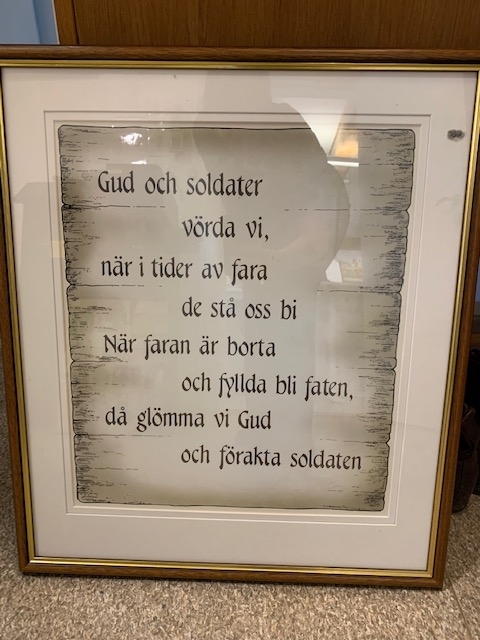 Tavla med glas och ram med texten:
"Gud och soldater vörda vi, när i tider av fara de stå oss bi. När faran är borta och fyllda bli faten, då glömma vi Gud och förakta soldaten"