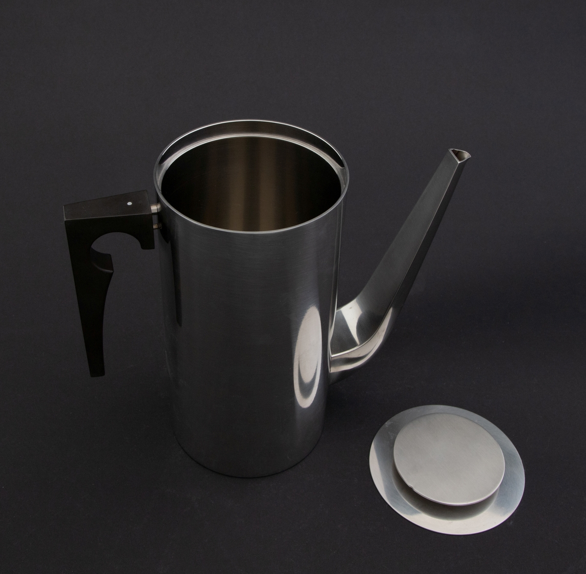 Cylinda-line kaffekanne i rustfritt stål med håndtak av svart kunstsstoff. Korpus er høy, sylinderformet med lang tut som er festet nederst på korpus. Lokket er løst med en sirkulær, flat lokknapp.