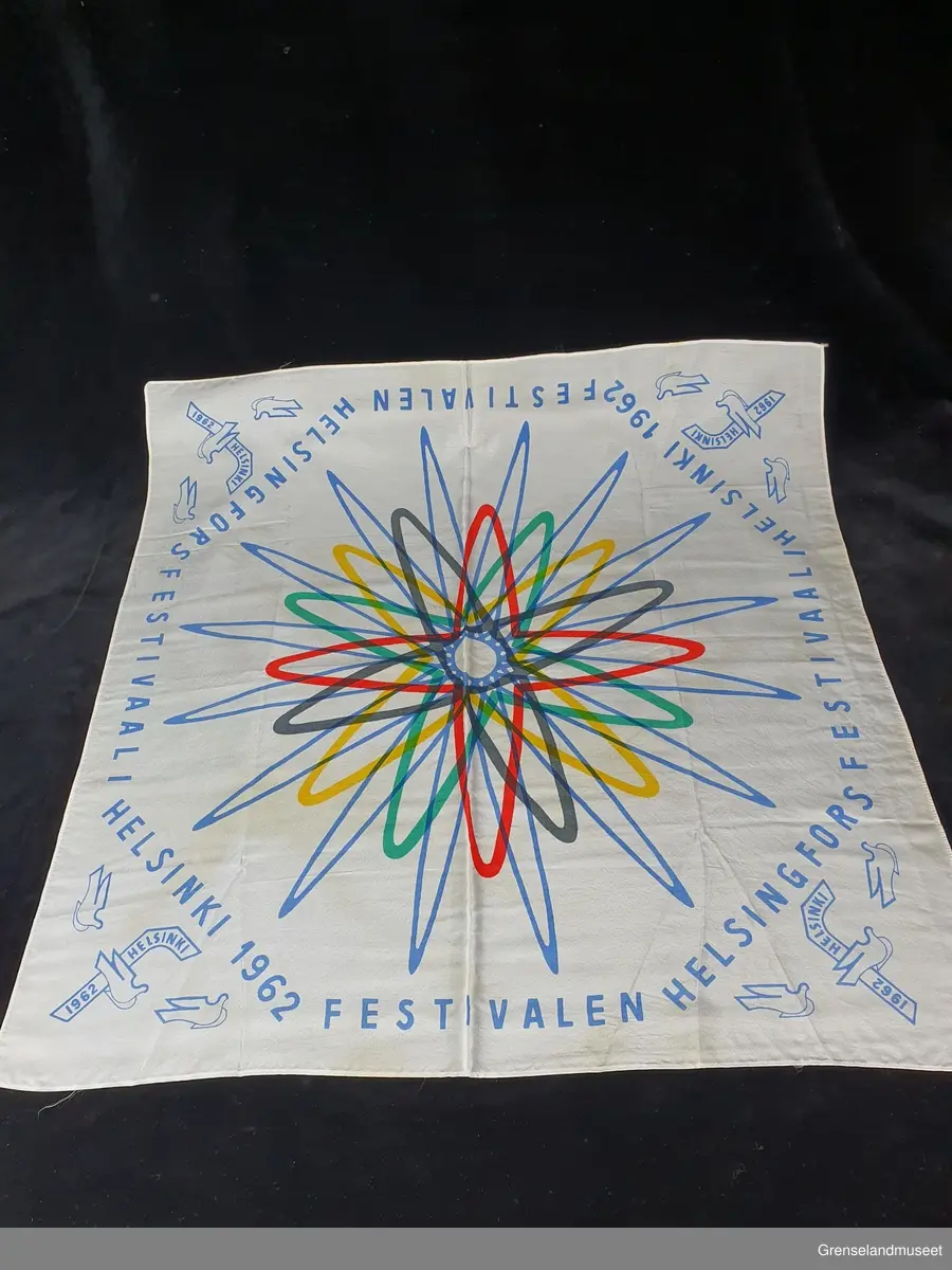 Hvit silke. Kvadratisk. Trykt mønster i blå, rød, grønn, gul, sort. Buer og spisser. Festivalen i Helsingfors 1962.