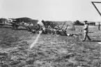 Flygplan J 2 nummer 67 står på Flygkompaniets flygfält på Malmen efter explosion vid luftpåfyllning den 15 augusti 1926. Två militärer bredvid flygplanet. I bakgrunden syns flyplan J 2 nummer 617 och 621.