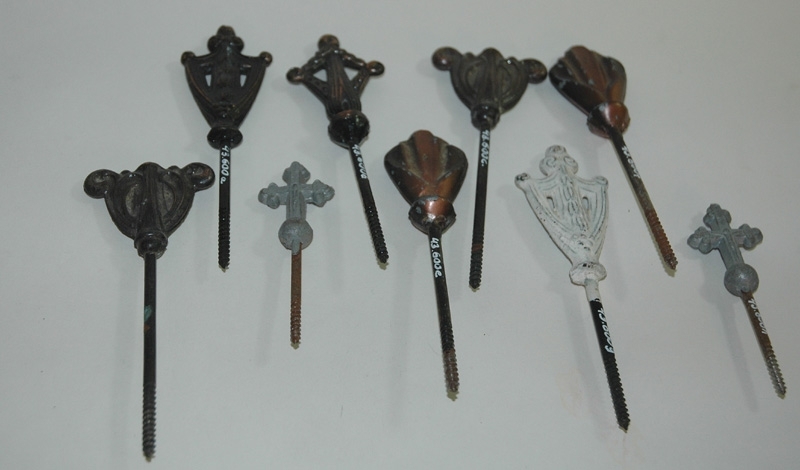 Olika typer av kistlås av metall. a) Måtten avser denna. b) Mått: 130x45 c) Mått: 130x50 d) Mått: 130x50 e) Mått: 130x35 f) Mått: 130x35 g) Vitmålat kistlås. Mått: 130x40 h) Silverfärgat kistlås i form utav ett kors. Mått: 90x30. i) Silverfärgat kistlås i form utav ett kors. Mått: 90x30. 1950-tal. 